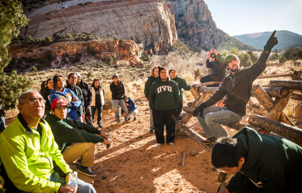 UVU students and faculty meet with members of the Mountain Ute tribe by the red sandstone cliffs of Capitol Reef National Park. Something off camera catches their gaze