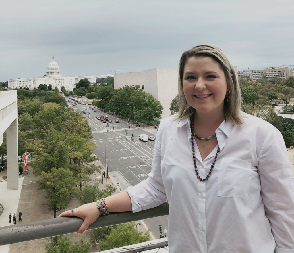 SMU junior Rylee Bailey poses against the railing of Washington D.C. balcony. Three blocks in the background, beyond a small forest of oak trees and bustling streets stands the ivory dome of the Capitol Building.